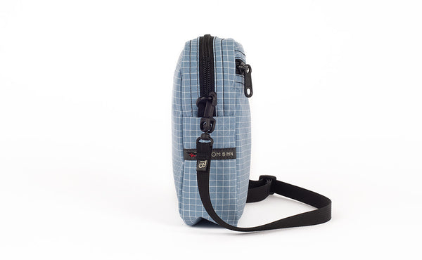 A side view of the Everyday Cubelet in Tidal Halcyon (faded blue with a white grid) showing the o-ring attachment point and included 5/8" strap.